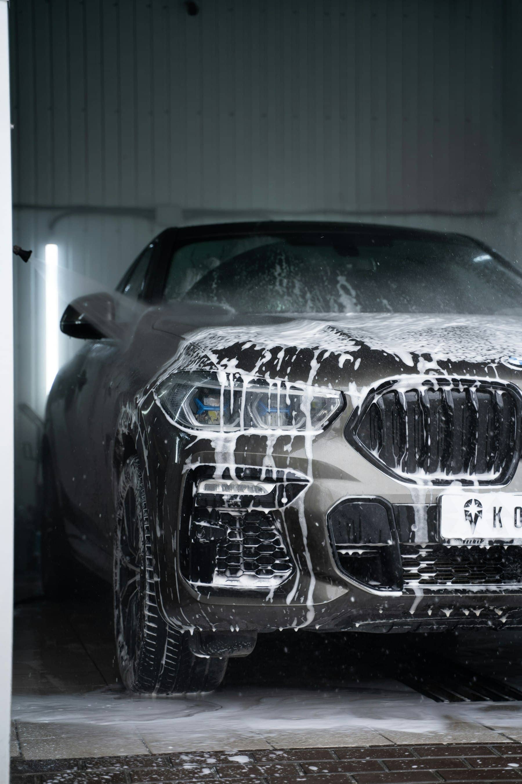 Front of a dark SUV covered in snow foam during exterior detailing