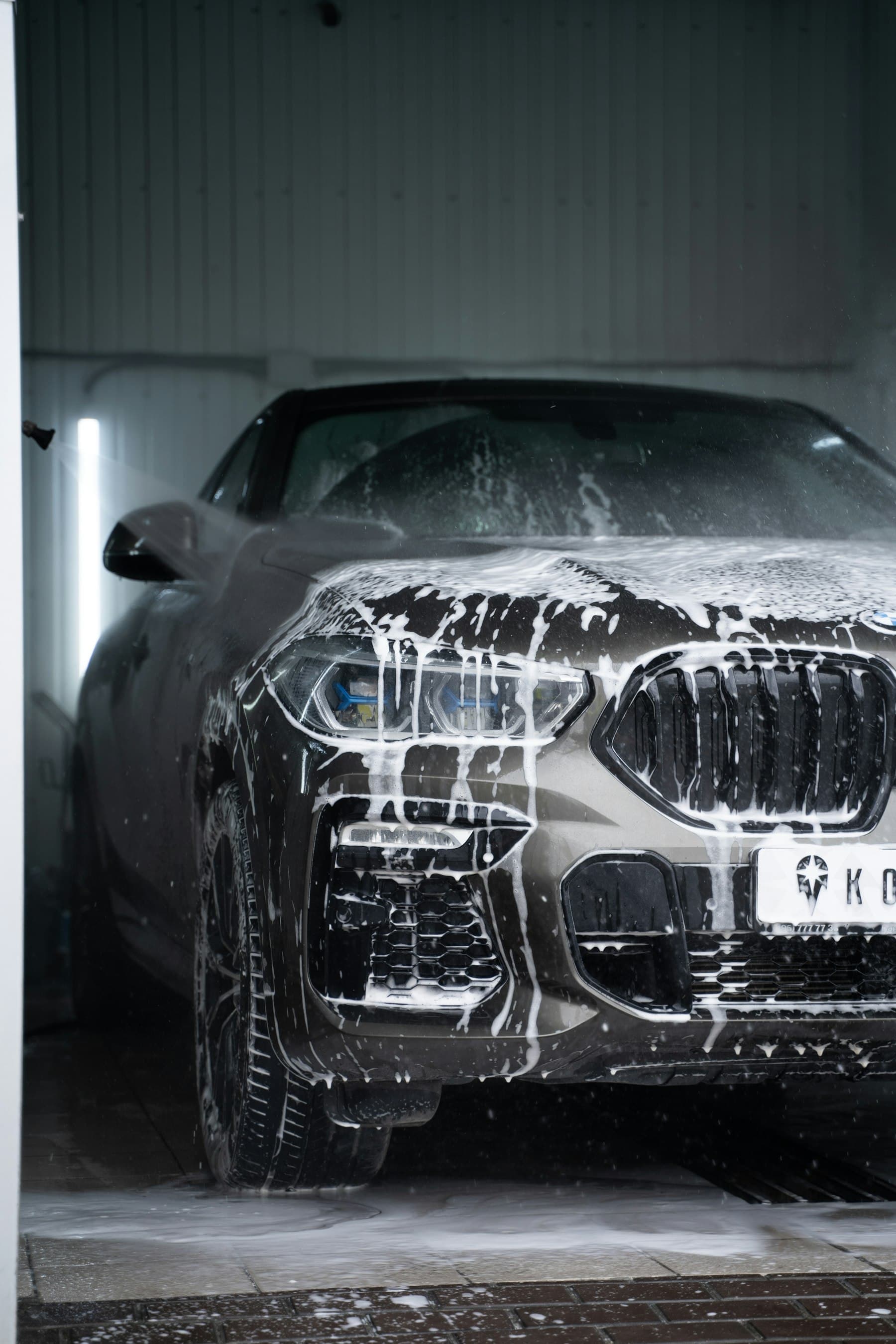 Front of a dark SUV covered in snow foam during exterior detailing