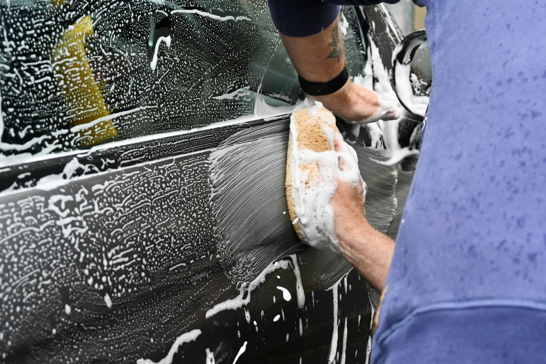 Hand washing a car door panel with a soapy wash mitt