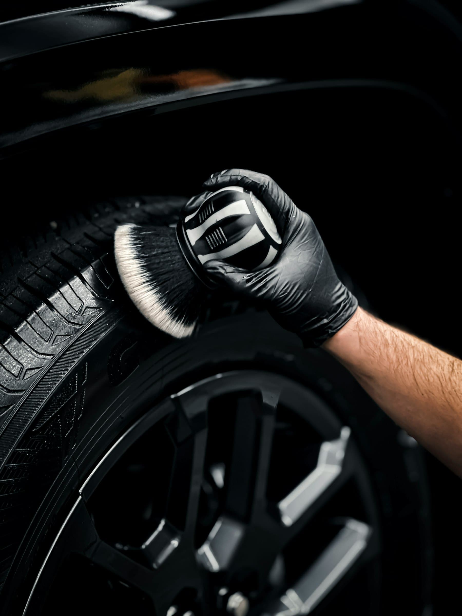 Gloved hand cleaning a car tyre and wheel with a detailing brush