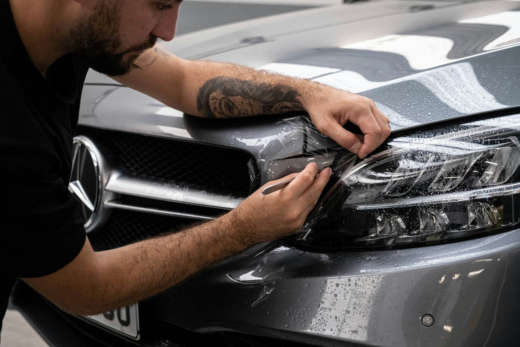 Installer fitting protective film around a car headlight