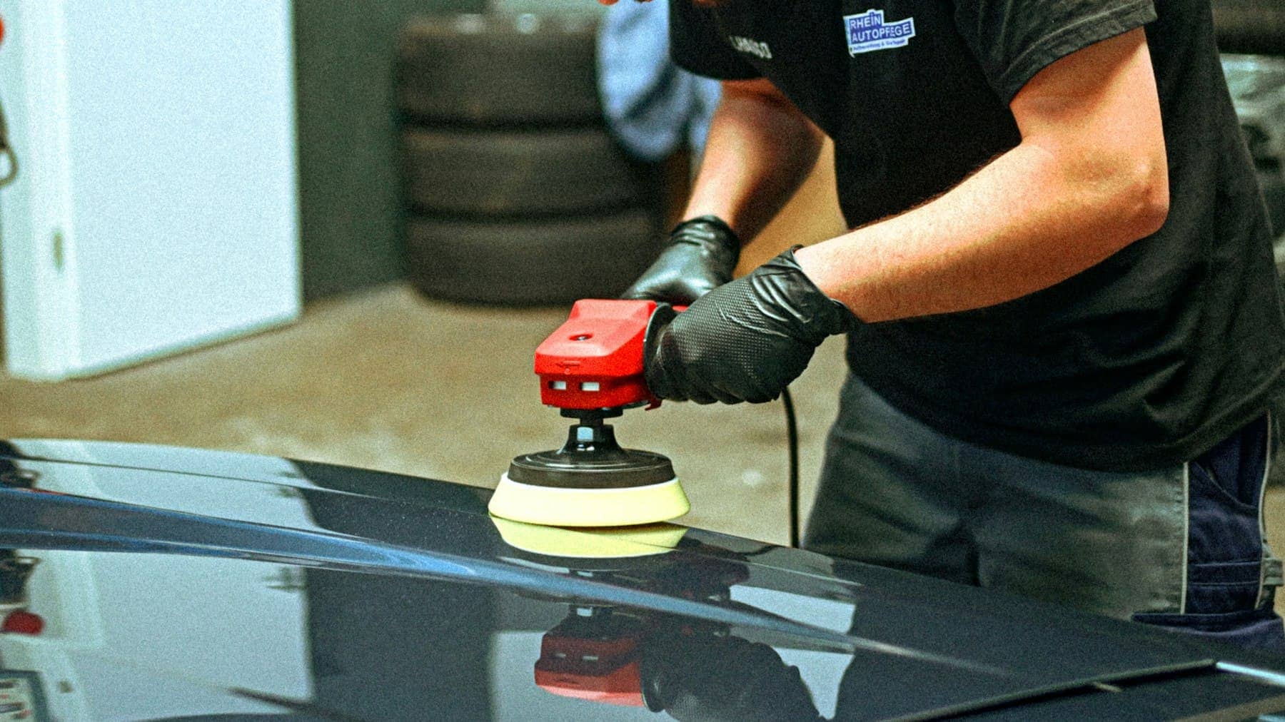 Technician polishing a dark car bonnet with an electric polisher