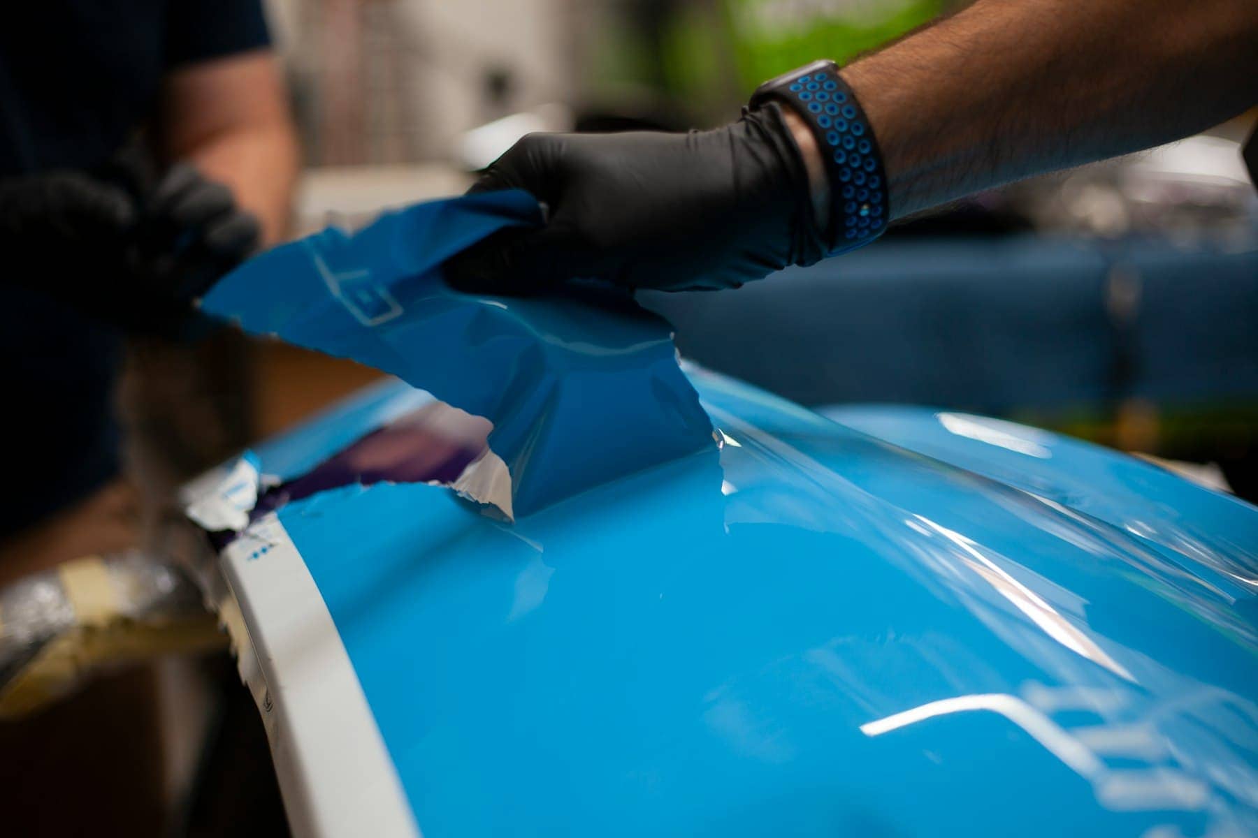 Installer applying clear protective film to a blue car panel